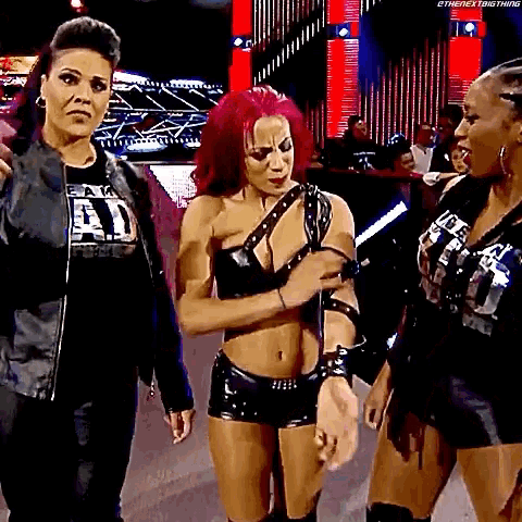 three women are standing next to each other on a stage in a wrestling ring .