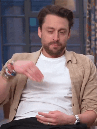 a man with a beard is sitting in a chair with his eyes closed and his hand on his stomach .