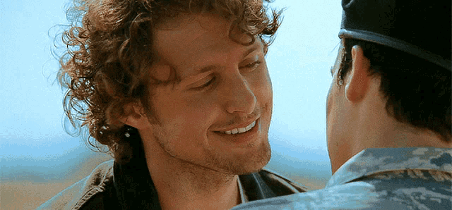 a man with curly hair is smiling while looking at another man