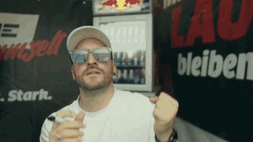 a man wearing sunglasses and a hat stands in front of a sign that says " lau bleiben "