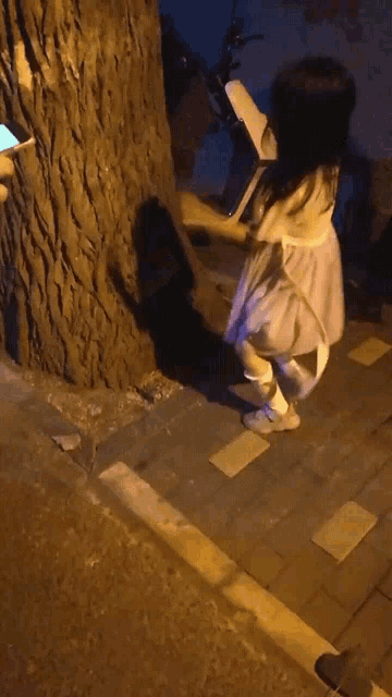 a little girl in a white dress is standing in front of a tree at night