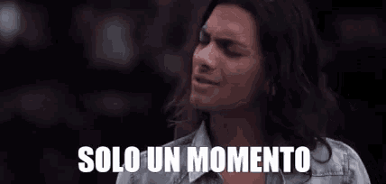 a man with long hair is standing in front of a sign that says solo un momento on it .