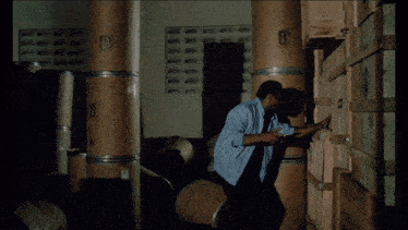 a man stands in a dark room surrounded by cardboard barrels and boxes with the letter b on them