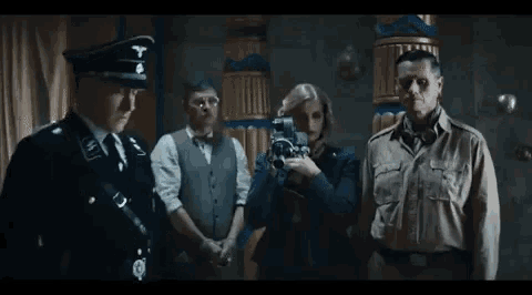 a woman is holding a camera in front of a group of men in uniforms .