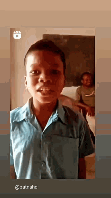 a young boy in a blue shirt is standing in front of a blackboard and smiling .