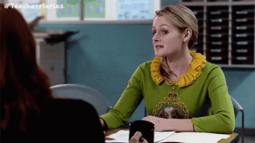 a woman in a green sweater is sitting at a desk with a cup of coffee .
