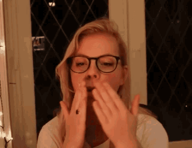 a woman wearing glasses and a white shirt is blowing her nose