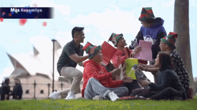 a group of people wearing santa hats are sitting on the grass holding gifts