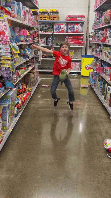 a young boy in a red shirt is jumping in the air in a toy store