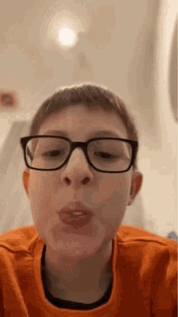 a young boy wearing glasses and an orange sweater is making a funny face .