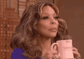 a woman in a blue dress is holding a pink mug of coffee .