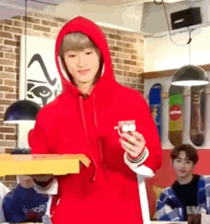a man in a red hoodie is holding a pizza box and a cup .