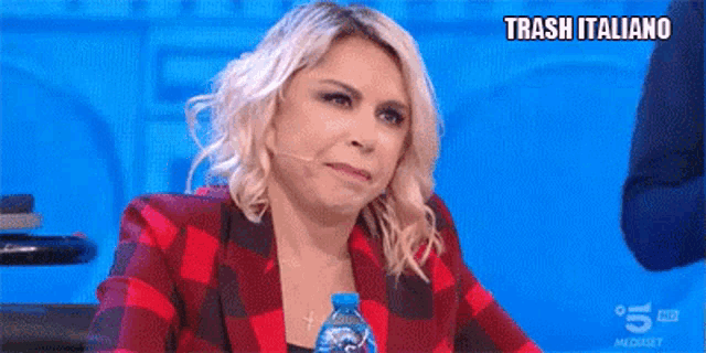 a woman in a red and black plaid jacket is sitting at a table with a bottle of water in her hand .