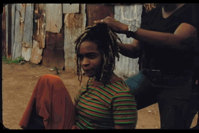a woman with dreadlocks is getting her hair braided by a man wearing a watch