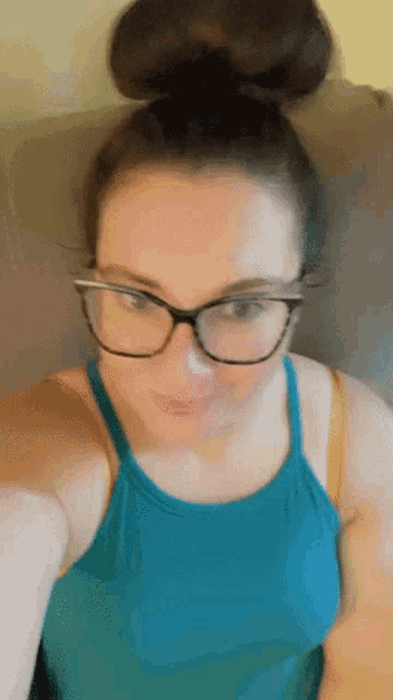 a woman wearing glasses and a blue tank top is taking a selfie