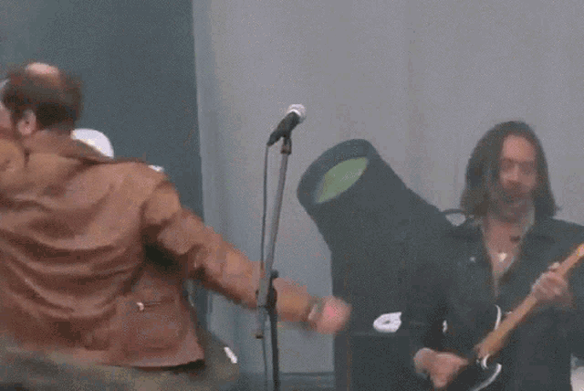 a man in a brown jacket is singing into a microphone with his arms in the air