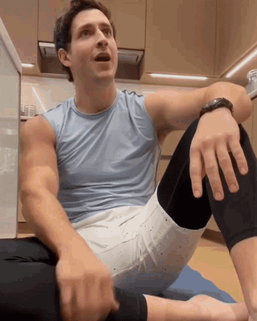a man in a blue tank top is sitting on the floor
