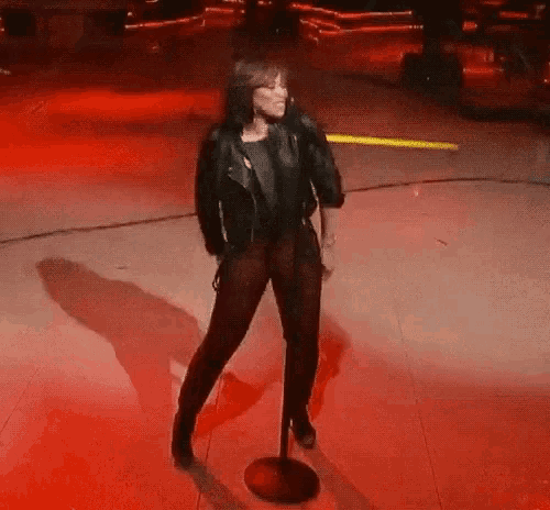 a woman in a black leather jacket is singing into a microphone on a stage .