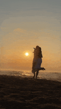 a man carrying a woman on his shoulders on the beach at sunset