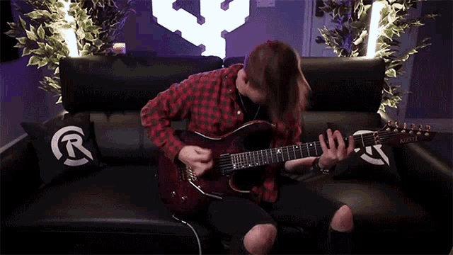 a man is playing a guitar on a couch with a pillow that says r