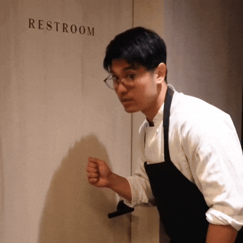 a man in an apron stands in front of a restroom sign