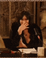 a woman covering her mouth with her hand while sitting at a table with a microphone .
