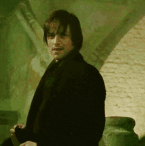 a man in a black jacket is standing in front of a brick wall and looking at the camera .