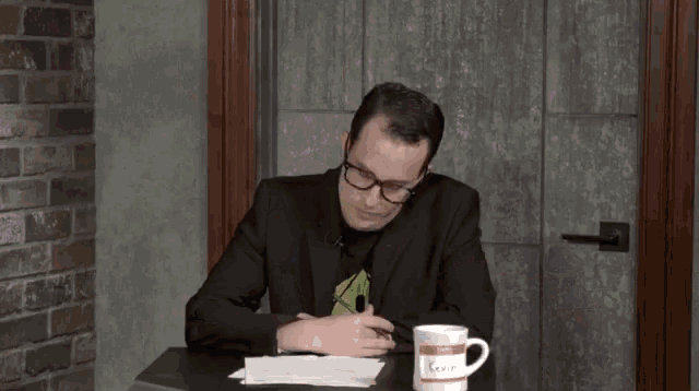 a man in a suit sits at a table with a coffee mug that says ' i love you ' on it