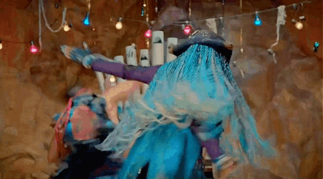 a woman in a blue dress is dancing with another woman in a purple dress in a cave .