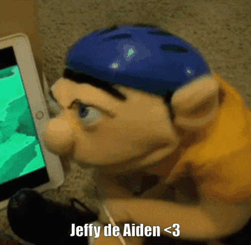 a puppet wearing a blue helmet is sitting in front of a tablet that says jeffy de aiden < 3 on it