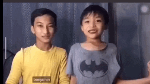 two young boys are standing next to each other and one of them is wearing a batman t-shirt .