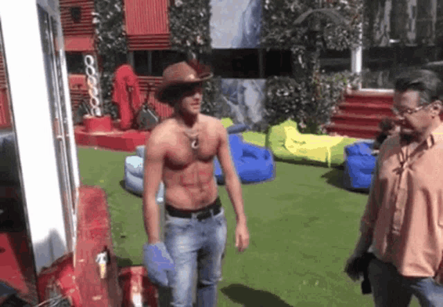 a shirtless man wearing a cowboy hat is standing next to another man
