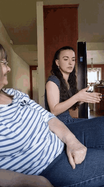 a woman in a blue and white striped shirt sits next to another woman in front of a black refrigerator