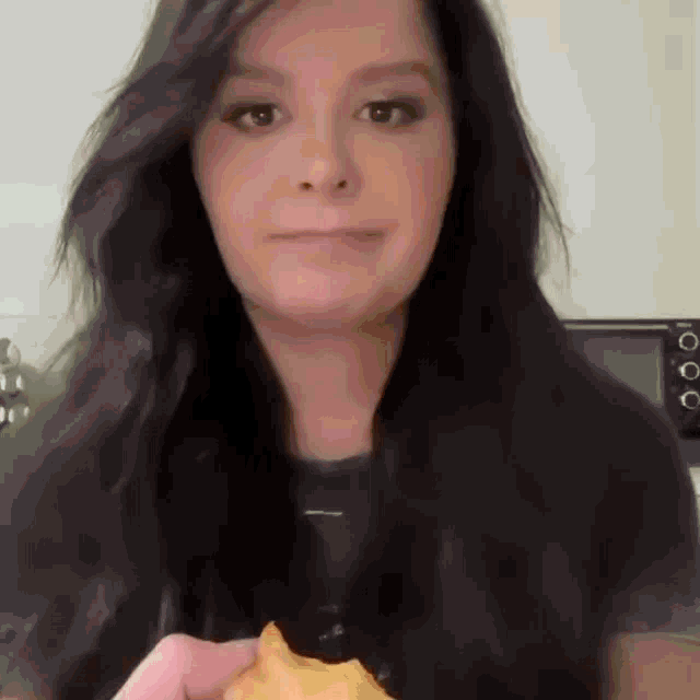 a woman with long black hair is holding a piece of food in front of her face .