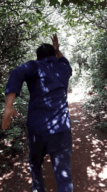 a man in a blue shirt is running through a lush green forest
