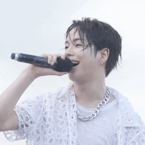 a man in a white shirt is singing into a microphone with his mouth open