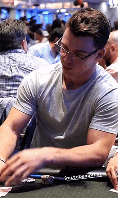 a man wearing glasses is sitting at a table with cards and chips