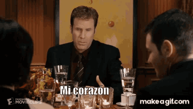 a man in a suit and tie is sitting at a table with a make a gif.com link below him