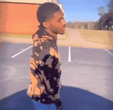 a young man wearing a tie dye sweatshirt stands in a parking lot