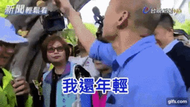 a man in a blue shirt stands in front of a crowd of people with chinese writing on them