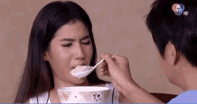a man is feeding a woman a spoon of food from a bowl