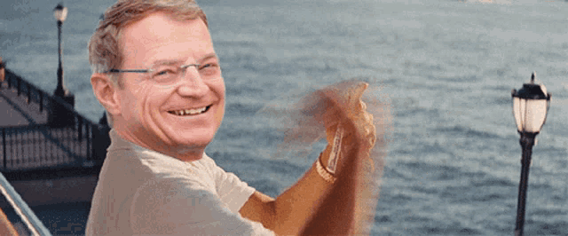 a man wearing glasses is smiling while looking out over a body of water