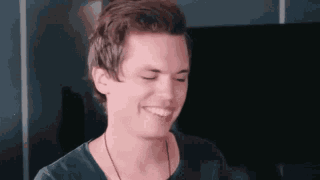 a young man is smiling with his eyes closed while wearing a necklace .
