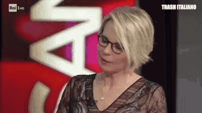 a woman wearing glasses is sitting in front of a red sign that says trash italiano