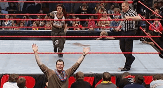 a wrestling ring with a referee and a man with his arms in the air