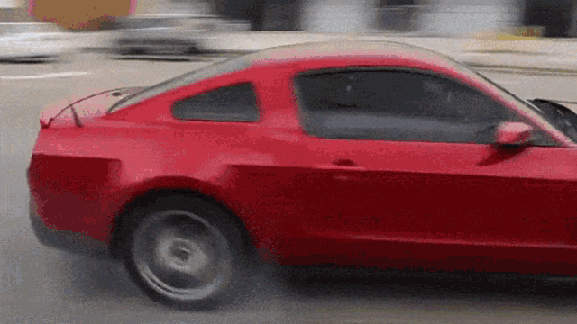 a red car is driving down a street with smoke coming out of its tire