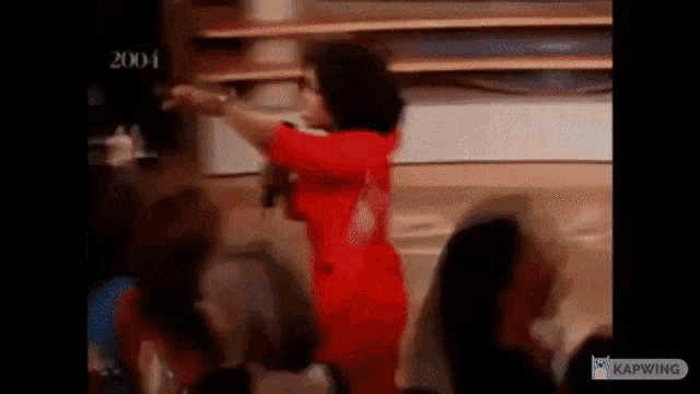 a woman in a red dress is dancing in front of a crowd of people in a room .