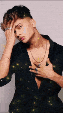 a young man wearing a black shirt and a necklace holds his hand to his face .