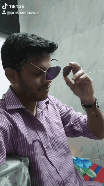 a man in a purple shirt is holding a pair of sunglasses in his hand