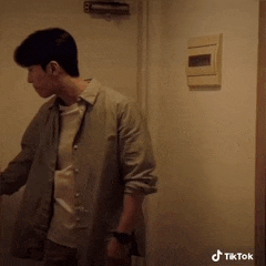 a man in a grey shirt is standing in a doorway next to a wall with a tiktok logo on it
